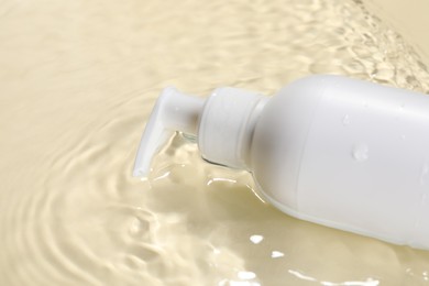 Bottle of face cleansing product in water against beige background, closeup. Space for text