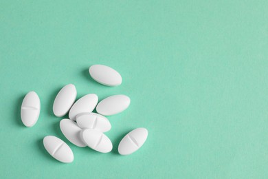 Pile of white pills on green background, flat lay. Space for text