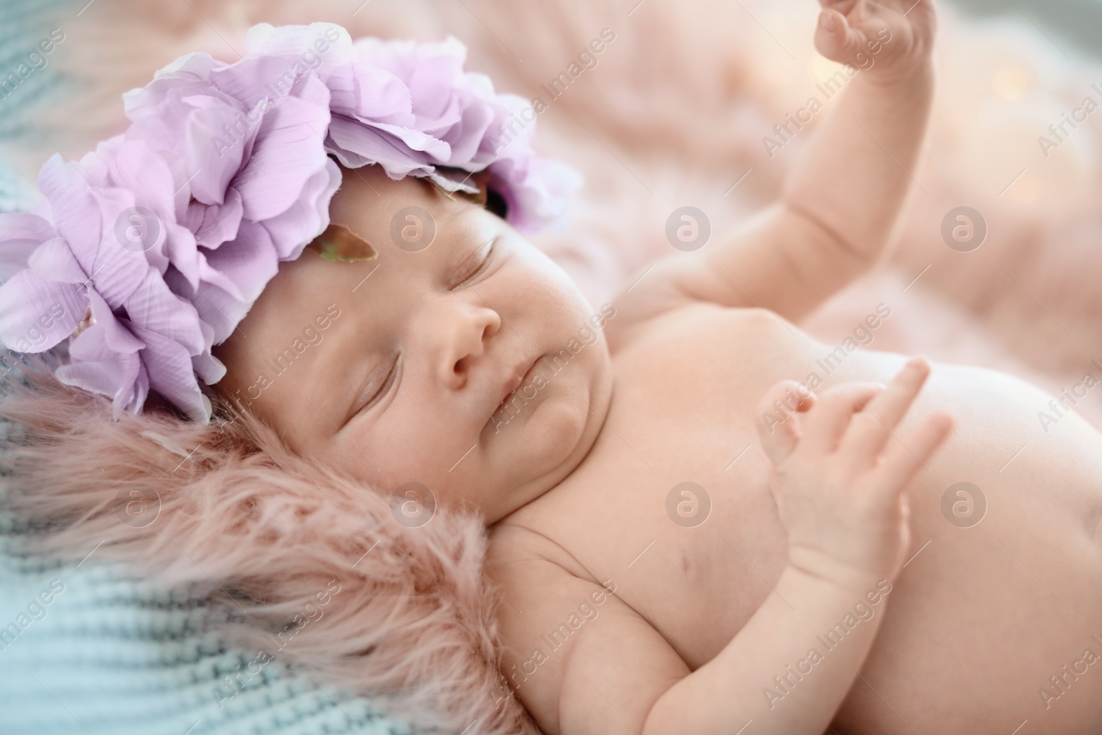 Photo of Adorable newborn baby girl with floral headband lying on bed