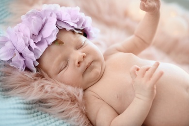 Adorable newborn baby girl with floral headband lying on bed