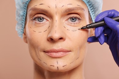 Photo of Doctor with marker preparing patient for cosmetic surgery operation on light brown background, closeup