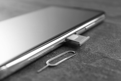 Photo of Mobile phone with Sim card in tray and ejector tool on grey table, closeup