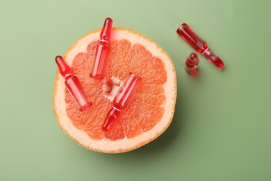 Photo of Skincare ampoules with vitamin C and half of grapefruit on light green background, top view