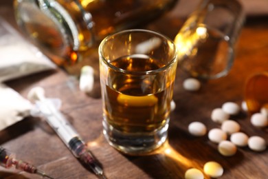 Photo of Alcohol and drug addiction. Whiskey in glass, syringes, pills and cocaine on wooden table, closeup