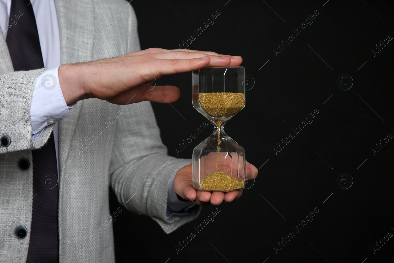 Photo of Closeup view of businessman holding hourglass on black background, space for text. Time management