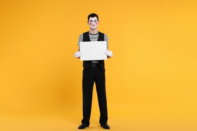 Photo of Funny mime artist with blank sign on orange background