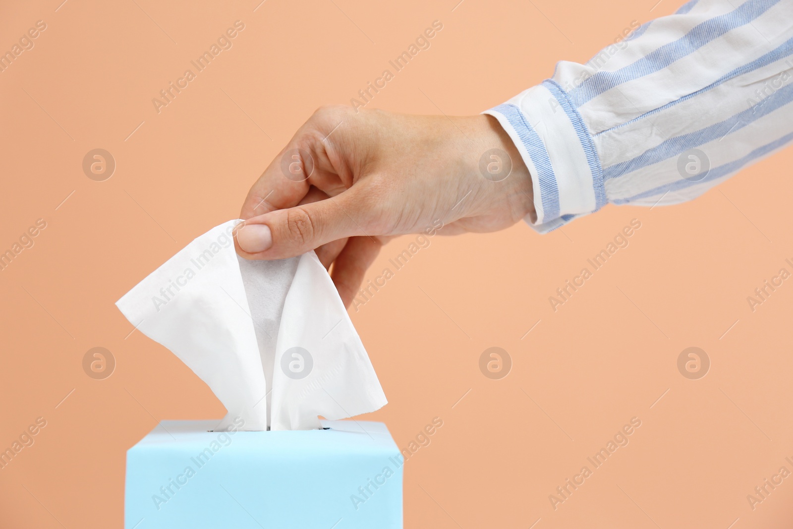 Photo of Woman taking paper tissue from box on light brown background, closeup