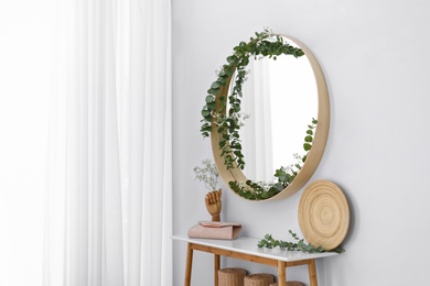 Photo of Round mirror and table with accessories near white wall. Modern interior design