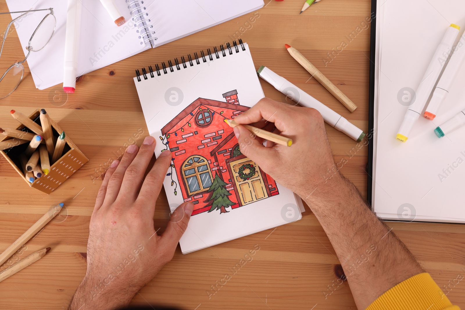 Photo of Man drawing in sketchbook with pencil at wooden table, top view