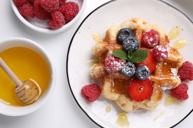 Photo of Delicious Belgian waffle with fresh berries and honey served on white table, flat lay