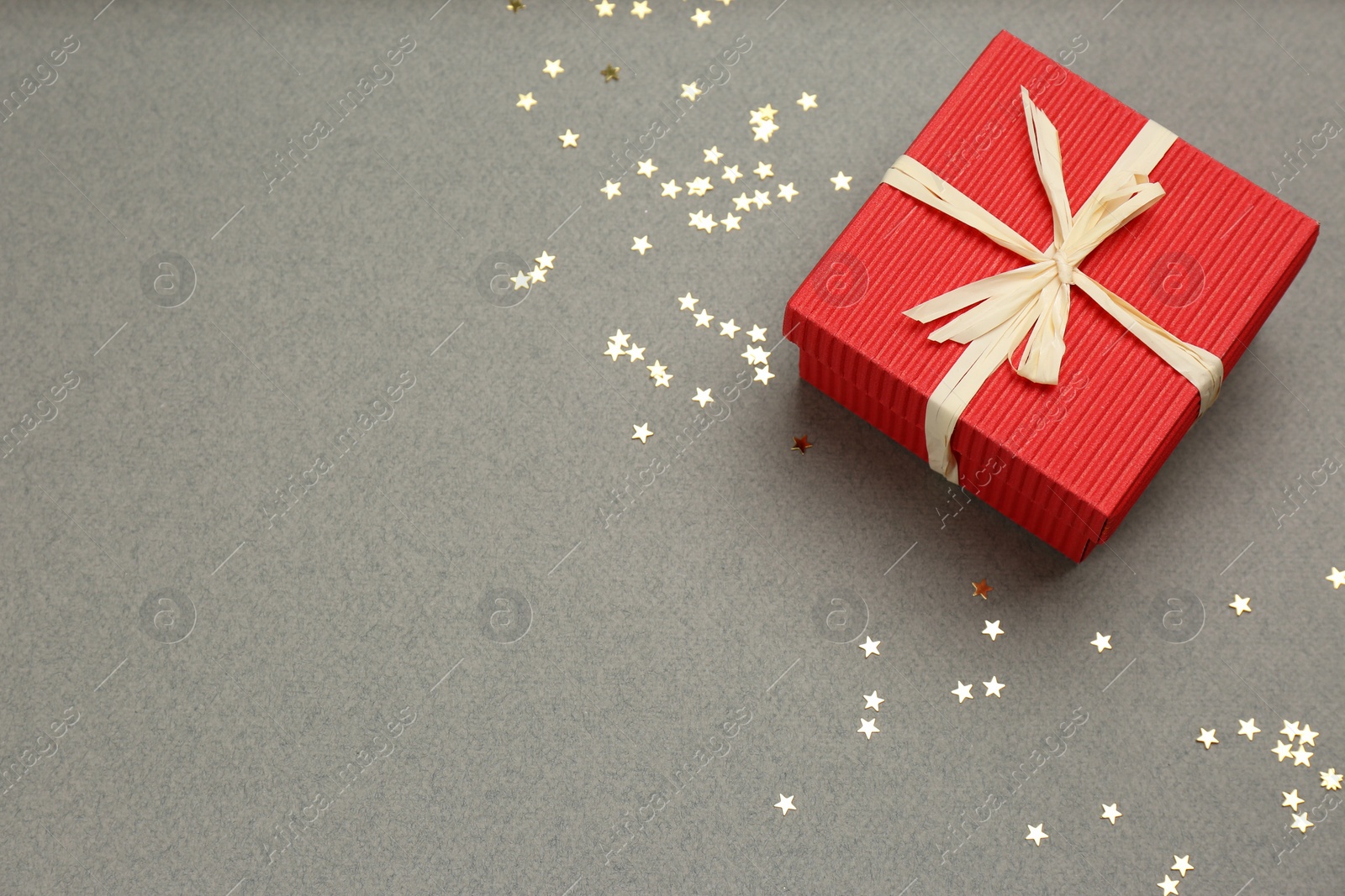 Photo of Red gift box and shiny confetti on grey background, above view. Space for text