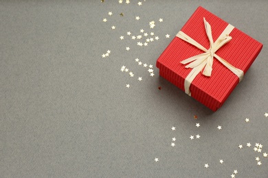 Photo of Red gift box and shiny confetti on grey background, above view. Space for text