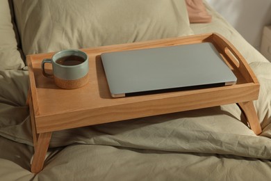 Photo of Wooden tray with modern laptop and cup of aromatic tea on bed indoors