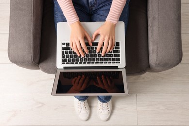 Photo of Woman working with laptop in armchair, top view