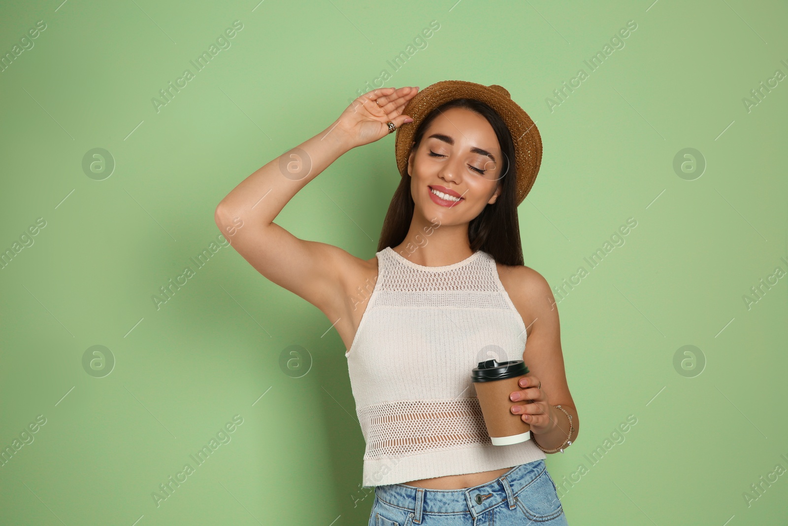 Photo of Beautiful young woman with straw hat and cup of coffee on olive background. Stylish headdress