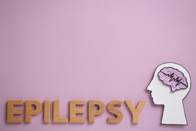 Photo of Word Epilepsy made of wooden letters near human head cutout with brain on pink background, flat lay. Space for text