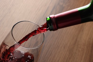 Pouring tasty red wine in glass at wooden table, closeup