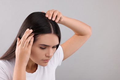 Photo of Woman examining her hair and scalp on grey background, closeup. Space for text