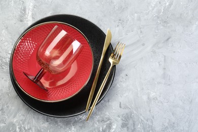 Photo of Clean plates, glass and cutlery on gray textured table, top view. Space for text