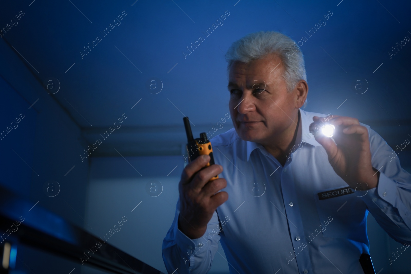 Photo of Professional security guard with portable radio set and flashlight in dark room