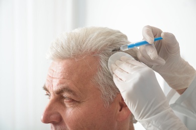 Senior man with hair loss problem receiving injection in salon, closeup