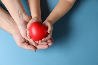 Photo of Father and his child holding red decorative heart on light blue background, top view. Space for text