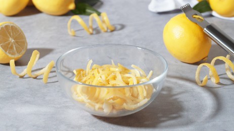 Photo of Bowl with peel pieces, fresh lemons and zester on grey table
