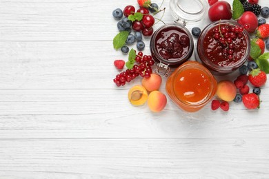 Photo of Jars with different jams and fresh fruits on white wooden table, flat lay. Space for text