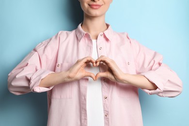 Photo of Woman making heart with hands on light blue background, closeup