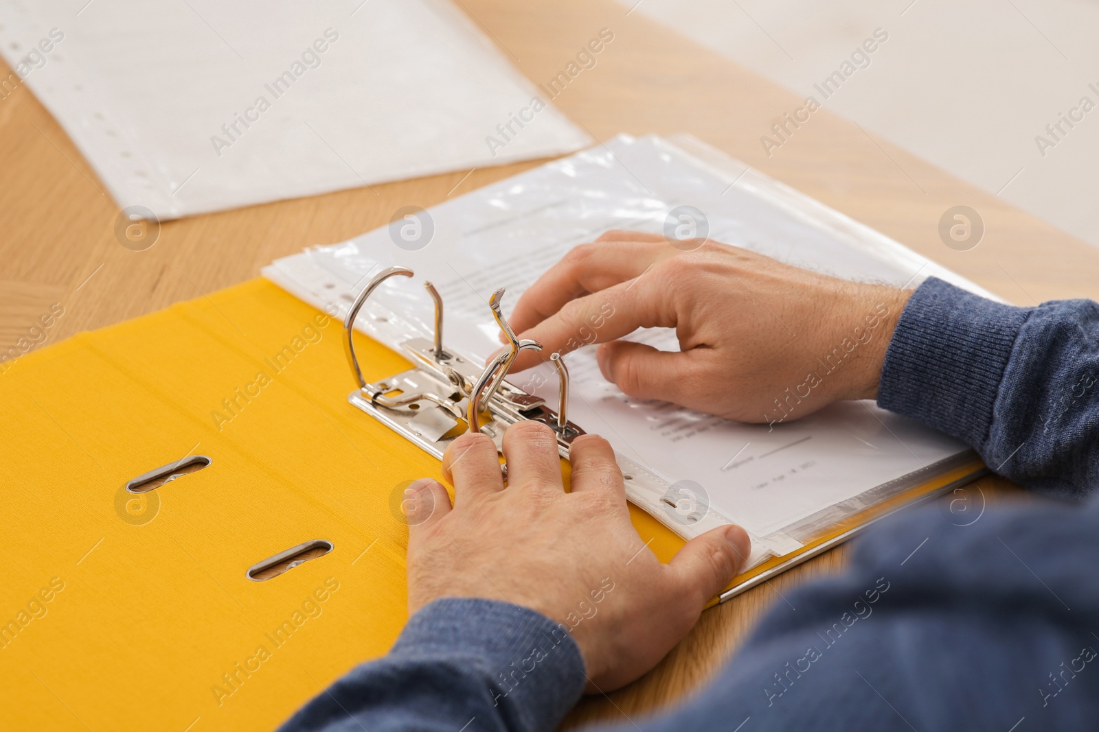 Photo of Businessman putting document into file folder at wooden table in office, closeup