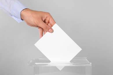 Photo of Man putting his vote into ballot box on light grey background, closeup