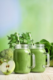 Photo of Mason jars of fresh green smoothie and ingredients on wooden table, space for text