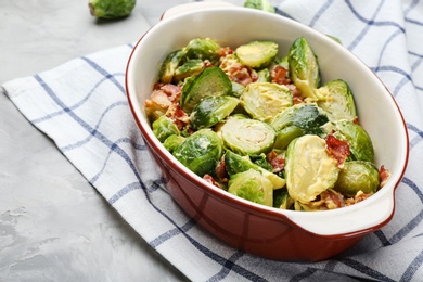 Photo of Delicious Brussels sprouts with bacon in baking pan on grey table, closeup