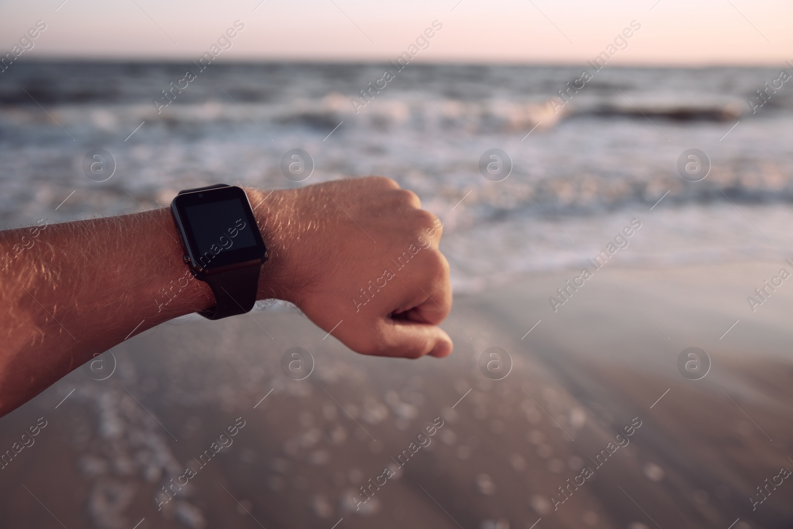 Photo of Man checking smart watch on beach at sunset, closeup