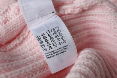 Clothing label with care symbols on pink sweater, closeup view