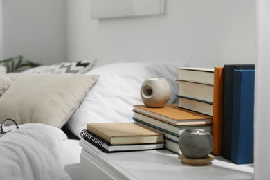 Photo of Hardcover books and scented candles on white bedside table in bedroom
