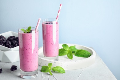 Photo of Delicious blackberry smoothie in glasses on light table. Space for text