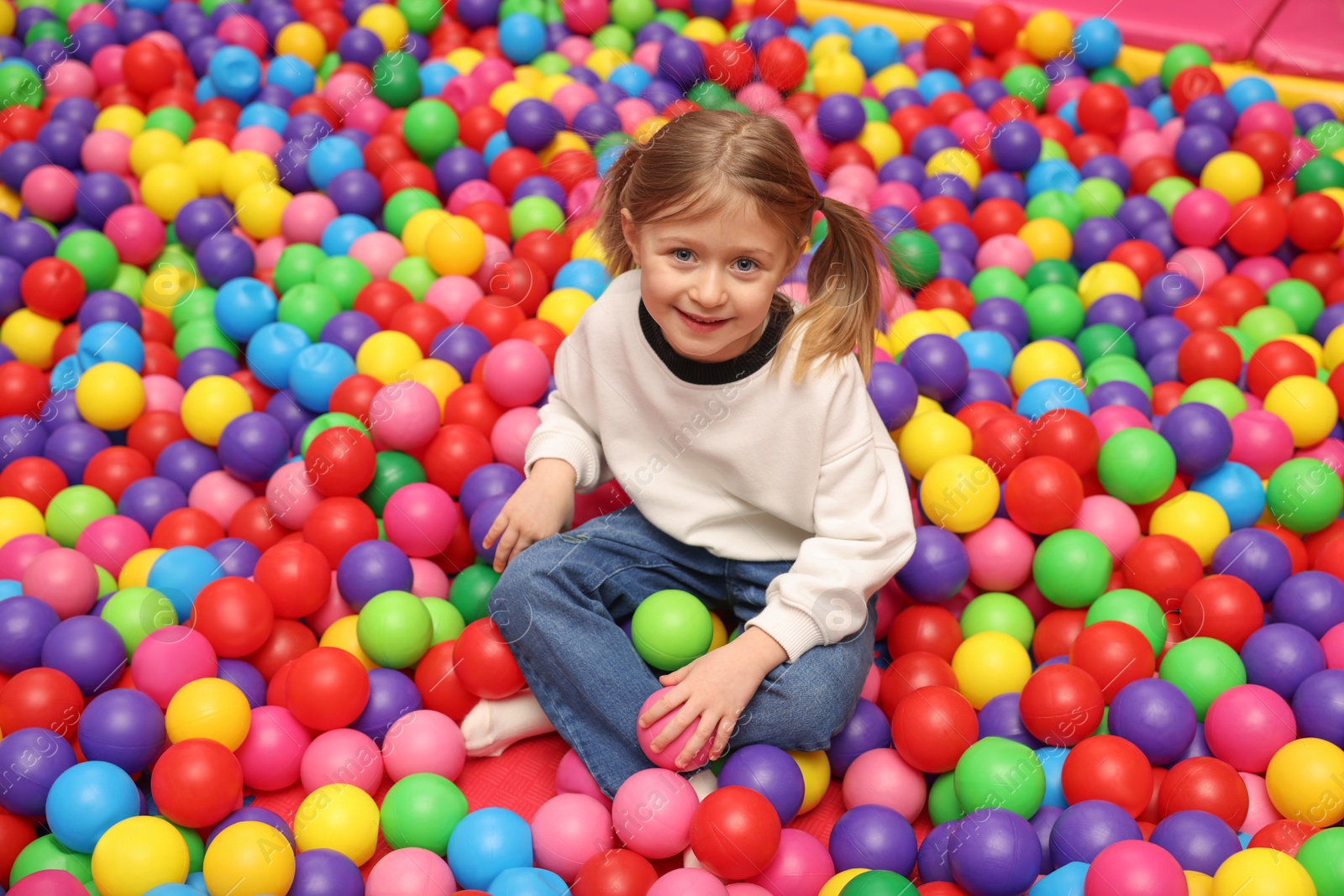 Photo of Happy little girl sitting on colorful balls in ball pit