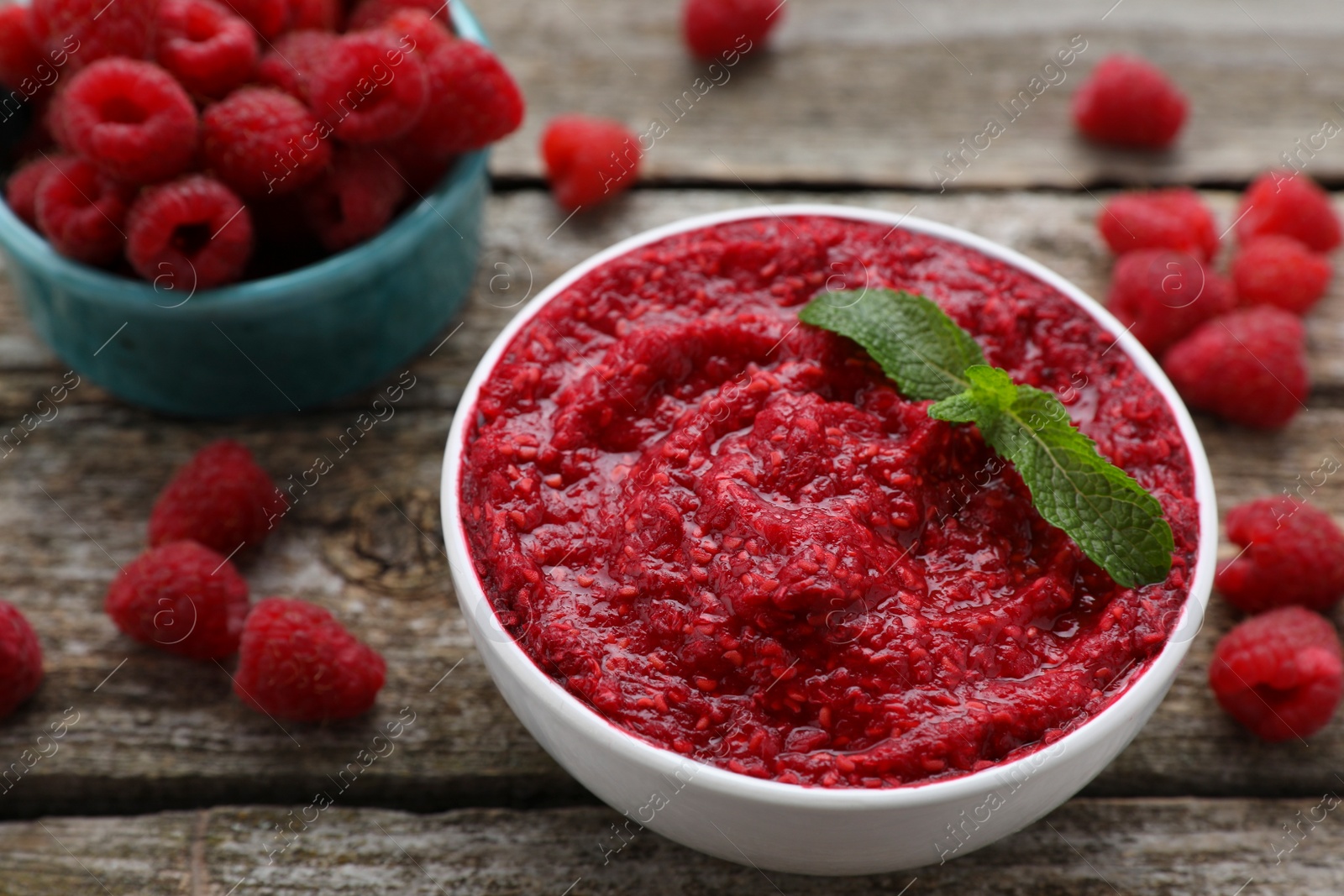 Photo of Raspberry puree in bowl and fresh berries on wooden table, closeup