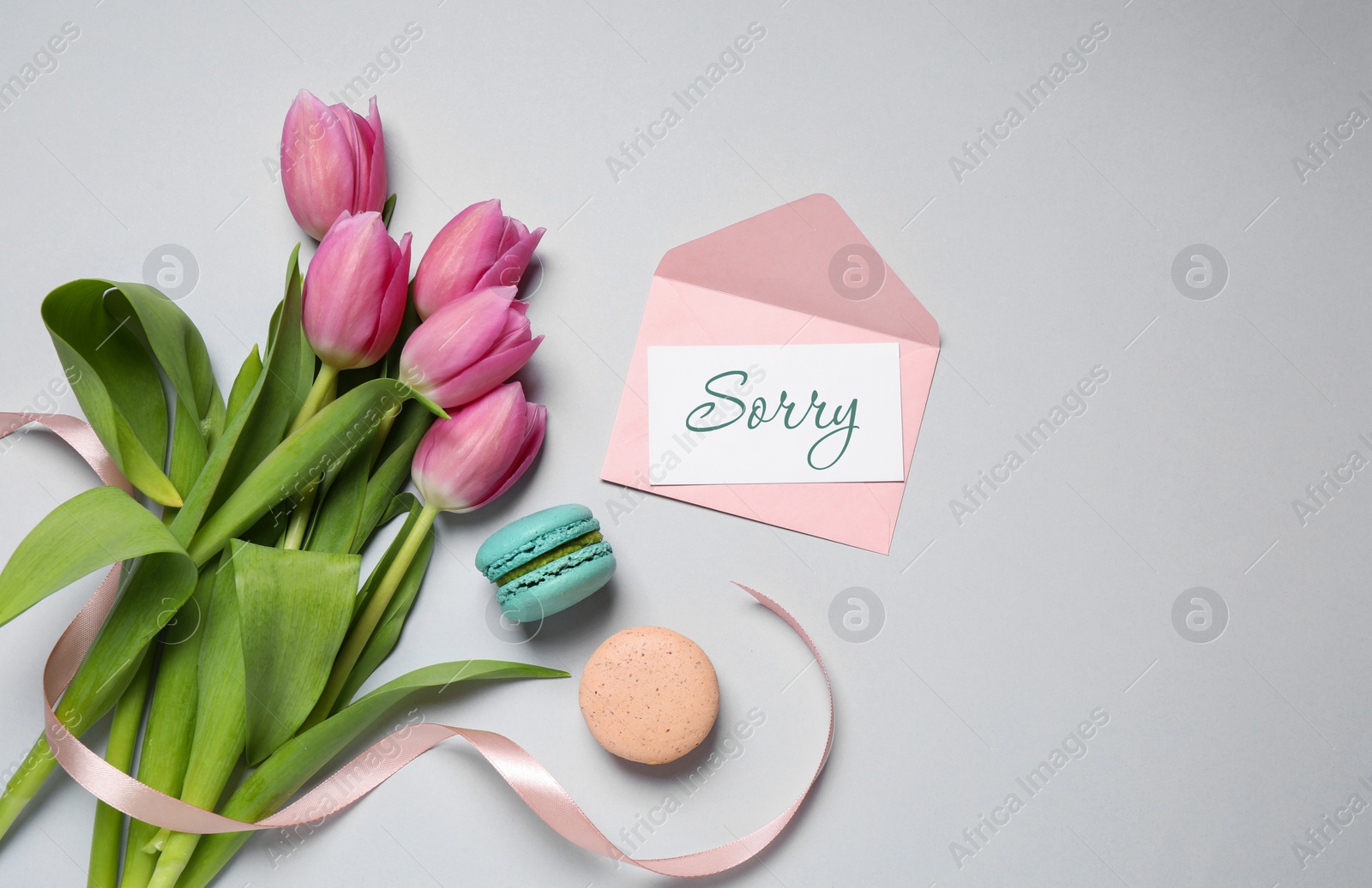 Image of Card with word Sorry, pink envelope, macarons and bouquet of tulips on light grey table, flat lay. Space for text