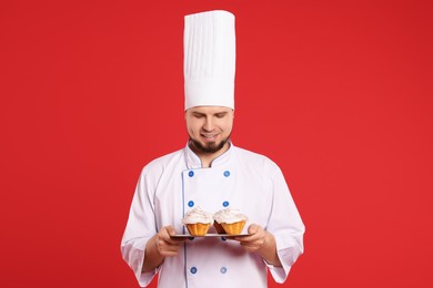 Happy professional confectioner in uniform holding delicious cupcakes on red background