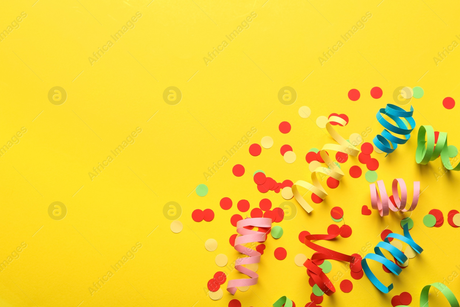 Photo of Colorful serpentine streamers and confetti on yellow background, flat lay. Space for text