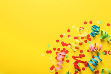 Photo of Colorful serpentine streamers and confetti on yellow background, flat lay. Space for text