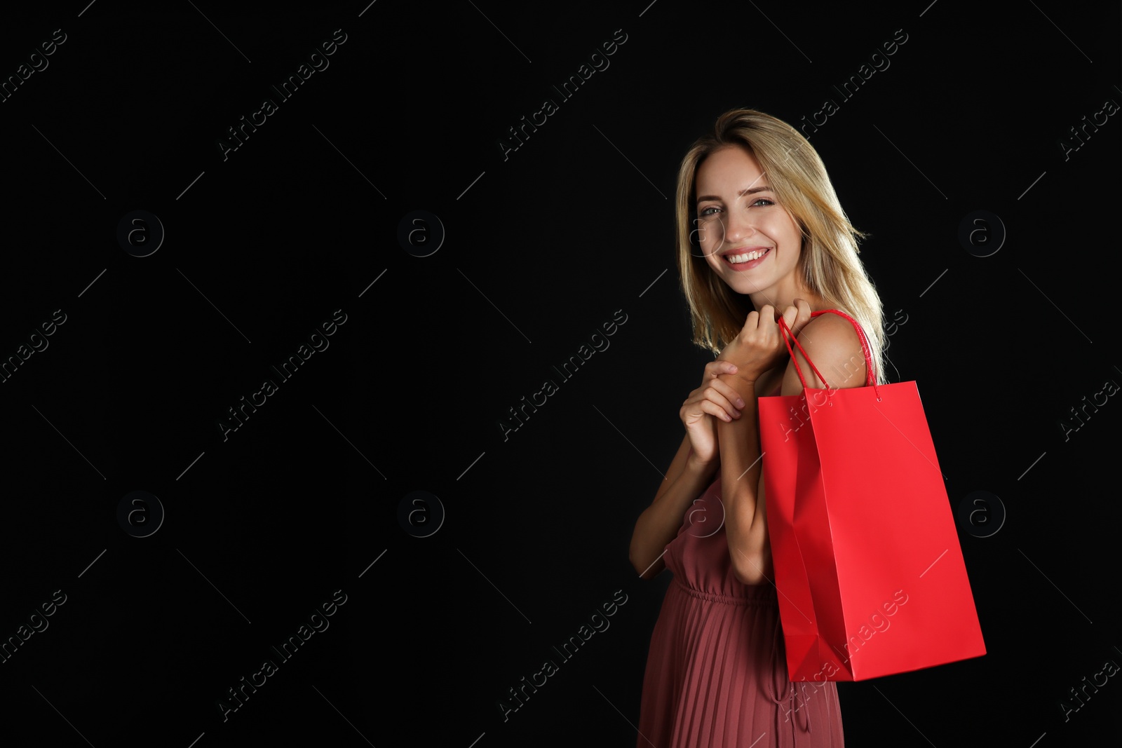 Photo of Happy young woman with shopping bag on dark background, space for text. Black Friday Sale
