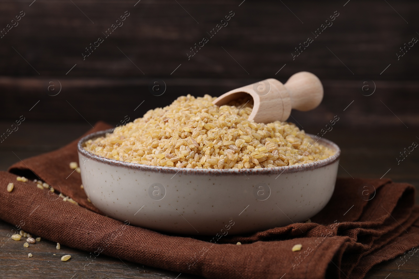 Photo of Bowl and scoop with raw bulgur on table, closeup