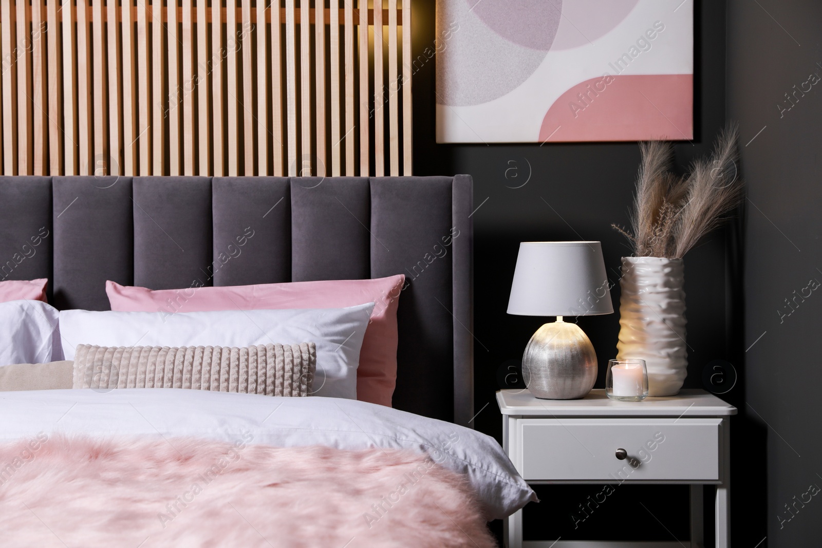 Photo of Comfortable bed with cushions, lamp and different decor on white bedside table in room. Stylish interior