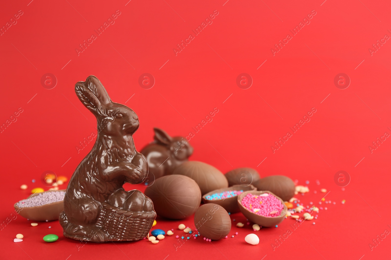 Photo of Chocolate Easter bunny, eggs and candies on red background. Space for text