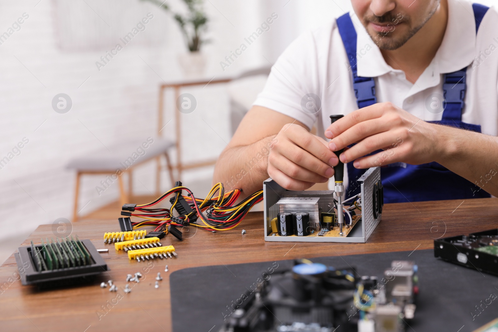 Photo of Male technician repairing power supply unit at table indoors, closeup