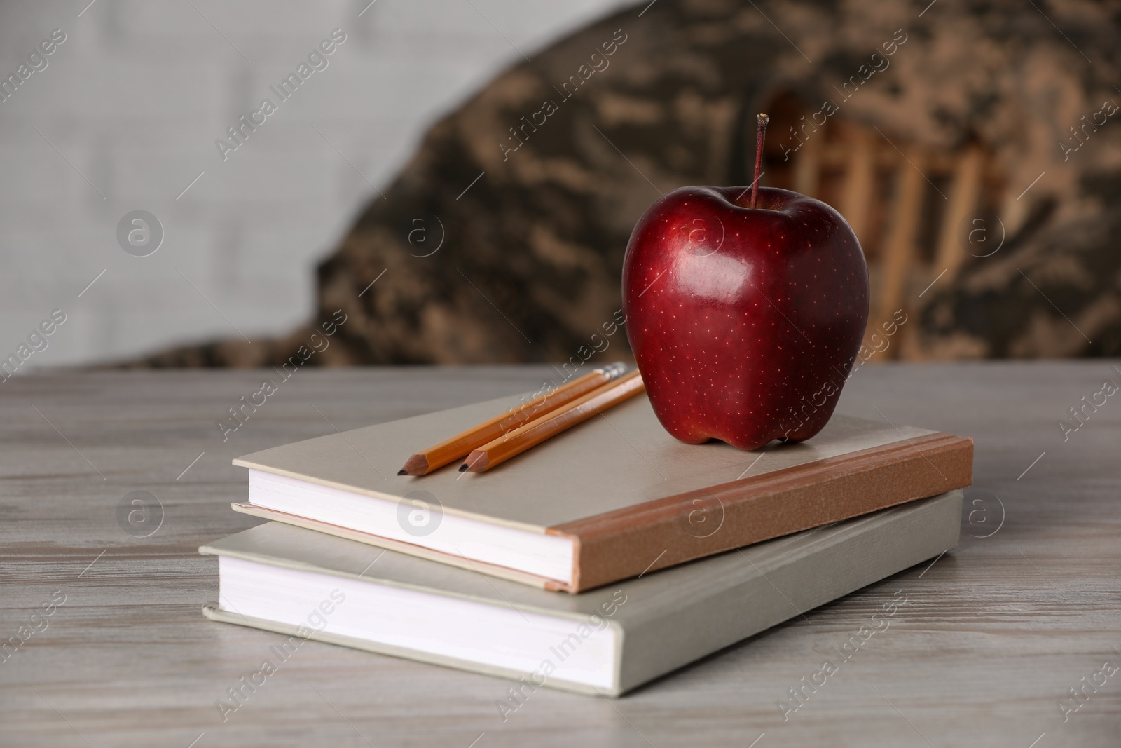 Photo of Notebooks, apple and pencils on wooden table. Military education