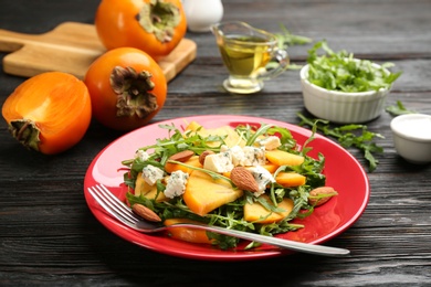 Photo of Delicious persimmon salad with blue cheese and arugula on wooden table